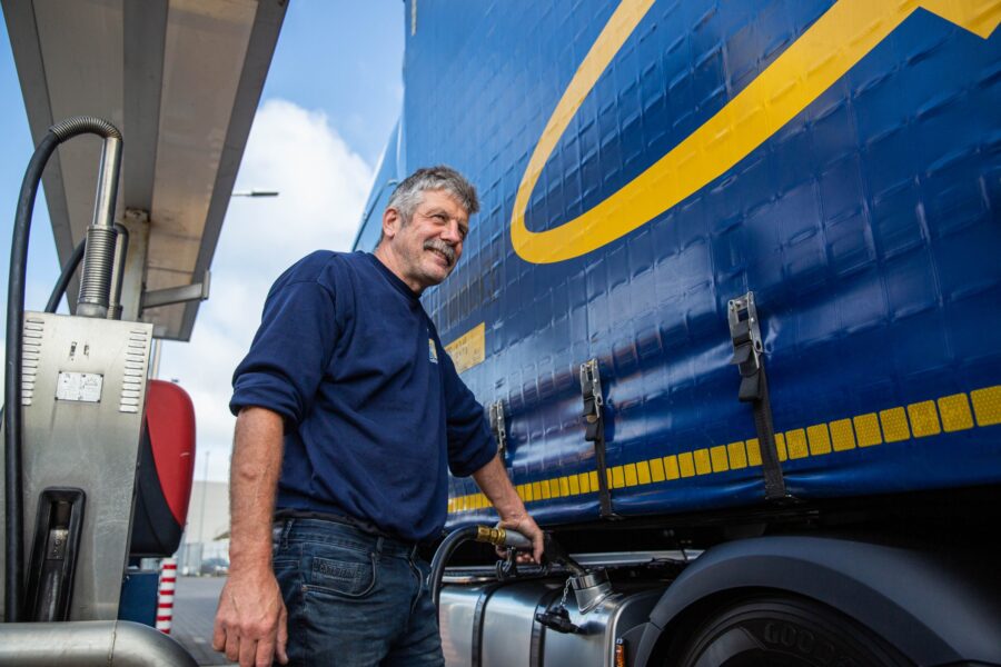 A driver is fueling up. He is laughing while looking away.