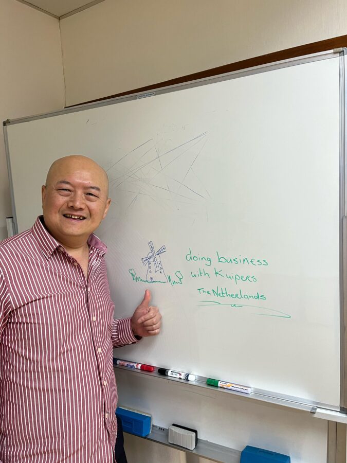 A proud partner of Kuipers Logistics stands next to a whiteboard. On the whiteboard is a drawing of a windmill with the text "doing business with Kuipers the Netherlands."