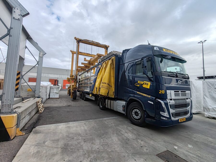 A tautliner with all curtains and the roof open. Goods are being lifted out from the top using a gantry crane.