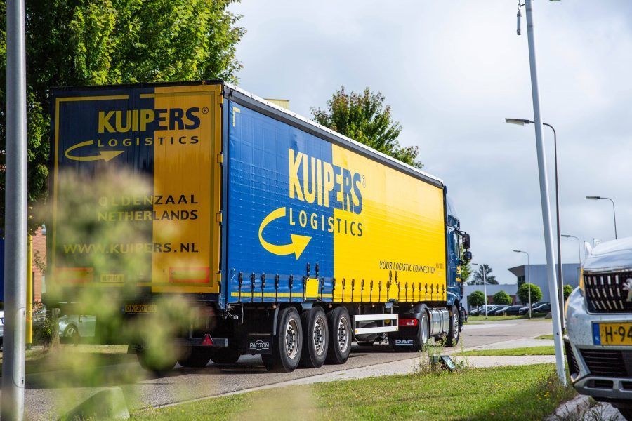 Een vrachtwagen met een trailer van Kuipers Logistics rijdt weg. De trailer is blauw met geel. Het is een tautliner die onder anderen geschikt is voor LTL transport. 