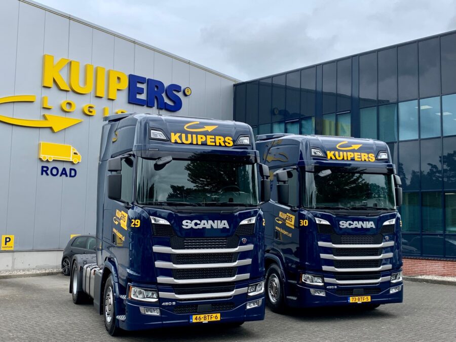 Twee Scania S450 Highline trucks in Kuipers huisstijl staan op de parkeerplaats voor het kantoor. 