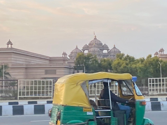 Tuk Tuk met geel dak en groene onderkant rijdt door New Delhi. Het presidentieel paleis is te zien op de achtergrond.