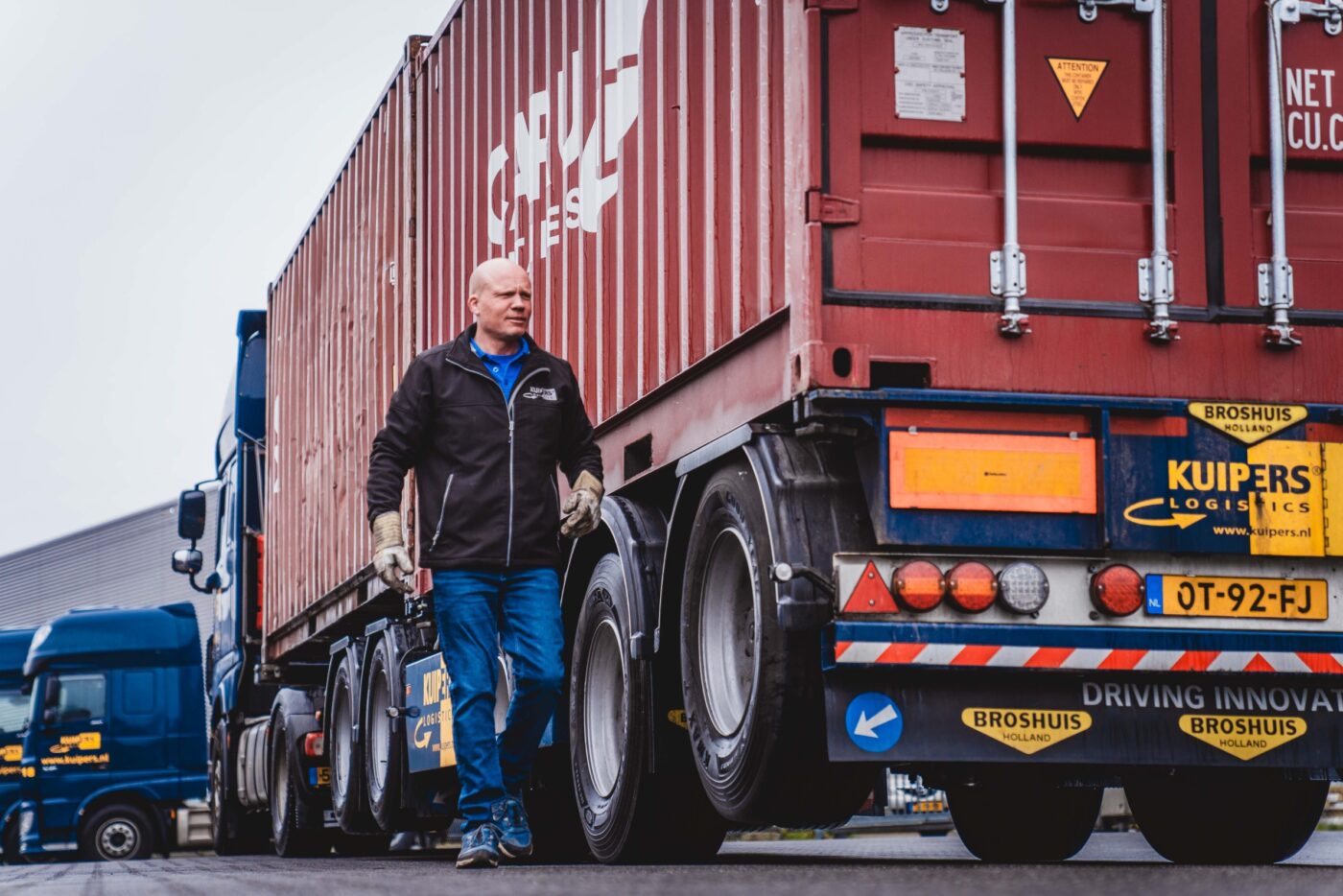 Een kale containerchauffuer loop naar de achterkant van een rode container die op een broshuis containerchassis van Kuipers Logistics staat.