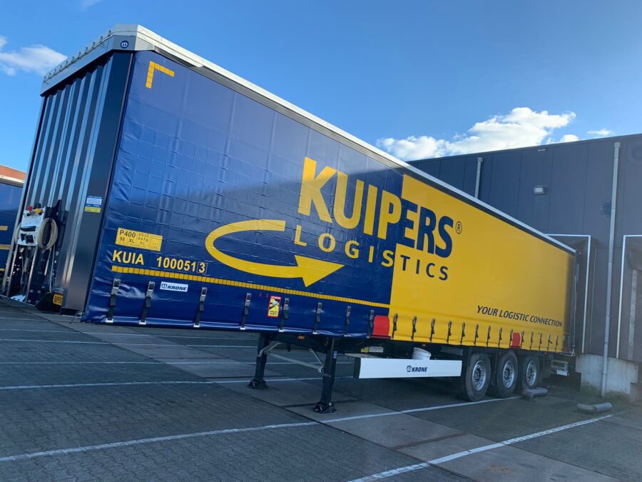 Op de foto is de rechter kant van een nieuwe KRONE Profi Liner SDP 27 eLHB50-CS van Kuipers Logistics te zien. de trailer staat aan het dok en is van een geel met blauwe opdruk voorzien.