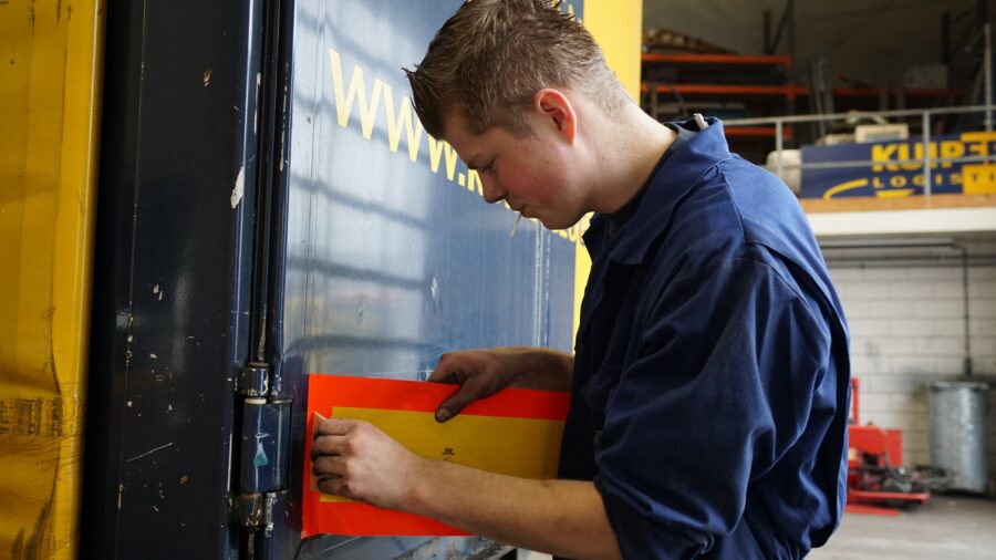 Een jonge Wouter, plakt een sticker op de achterkant van de Kuipers Logistics trailer