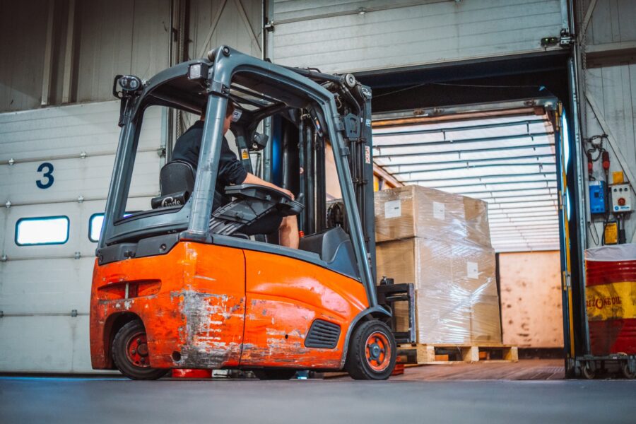 Een rode heftruck rijdt een pallet In vrachtwagen via een dock
