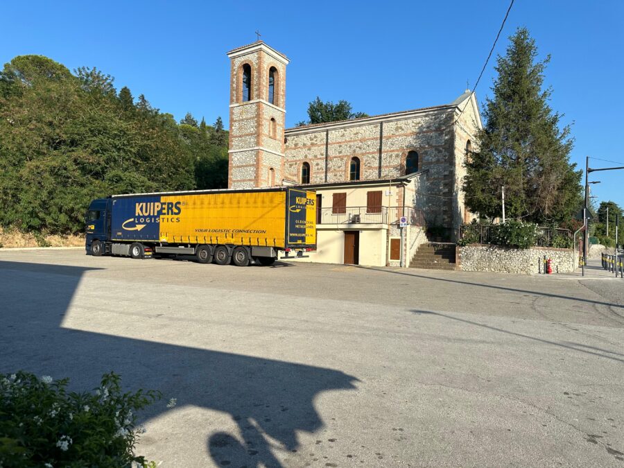 Een vrachtwagen van Kuipers Logistics staat voor een Kerkje in Rimini.